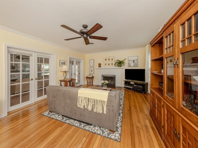 living room with crown molding, a fireplace, french doors, and light wood-type flooring