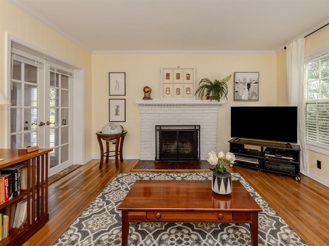 living room featuring a brick fireplace, wood-type flooring, ornamental molding, and french doors