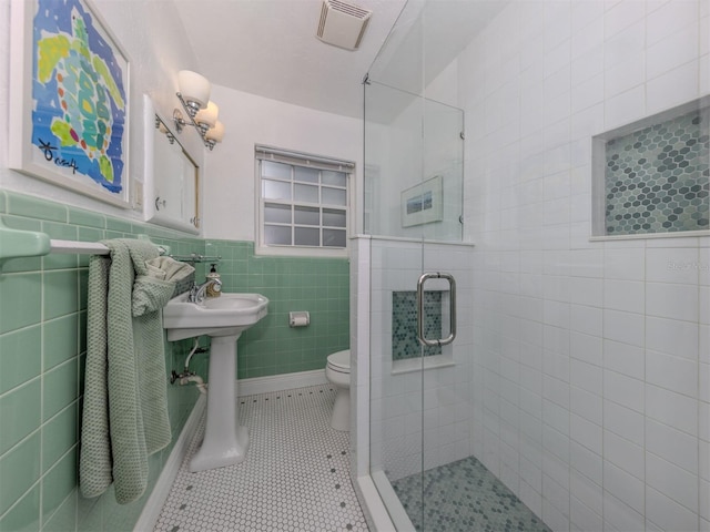 bathroom featuring a shower with shower door, sink, tile walls, toilet, and tile patterned floors