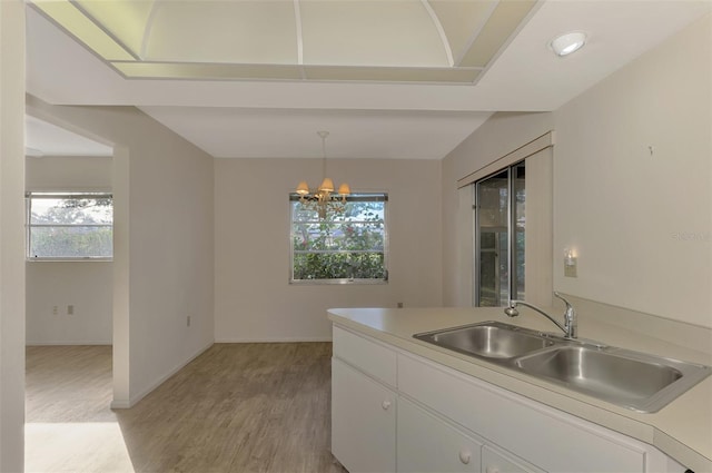 kitchen with decorative light fixtures, white cabinetry, sink, a chandelier, and light hardwood / wood-style flooring