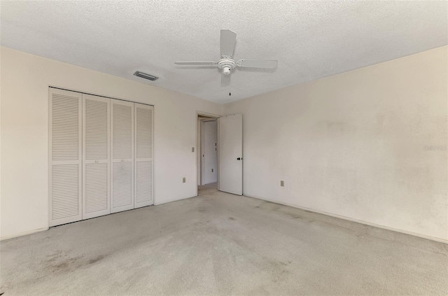 unfurnished bedroom with light carpet, a textured ceiling, a closet, and ceiling fan