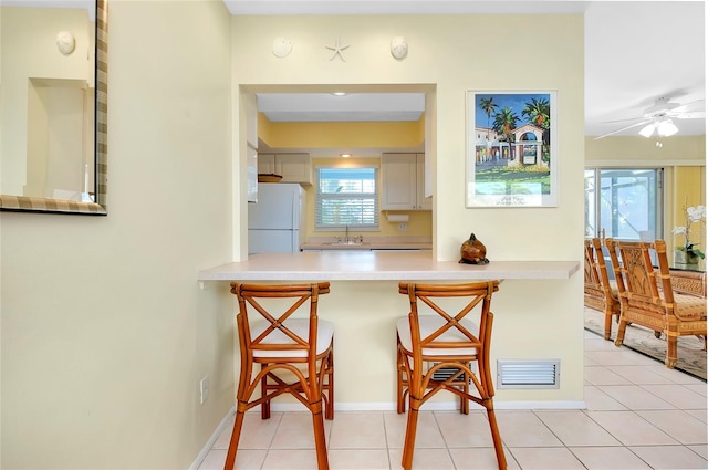 kitchen featuring light tile patterned floors, a wealth of natural light, a kitchen bar, and white fridge