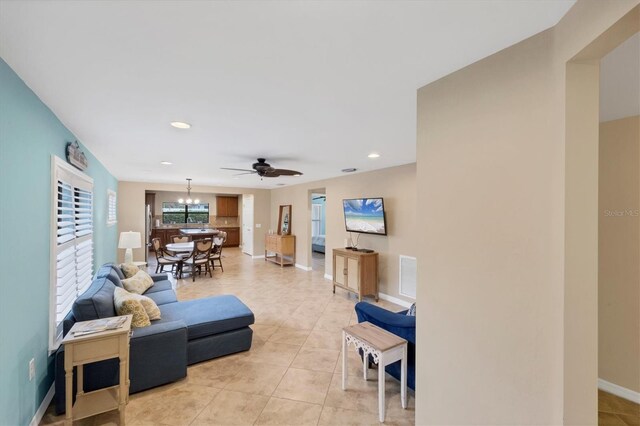 tiled living room with ceiling fan with notable chandelier