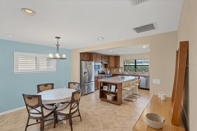 kitchen featuring light tile patterned floors, hanging light fixtures, stainless steel appliances, a notable chandelier, and a kitchen island