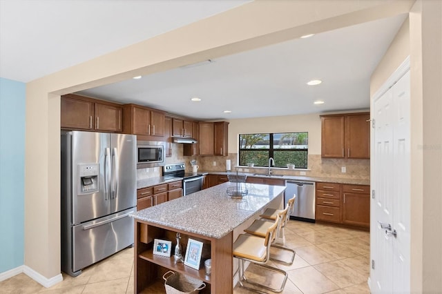 kitchen with tasteful backsplash, stainless steel appliances, a center island, and light stone countertops