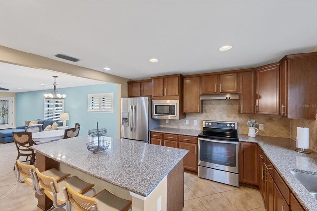 kitchen with a breakfast bar, hanging light fixtures, stainless steel appliances, a center island, and light stone countertops