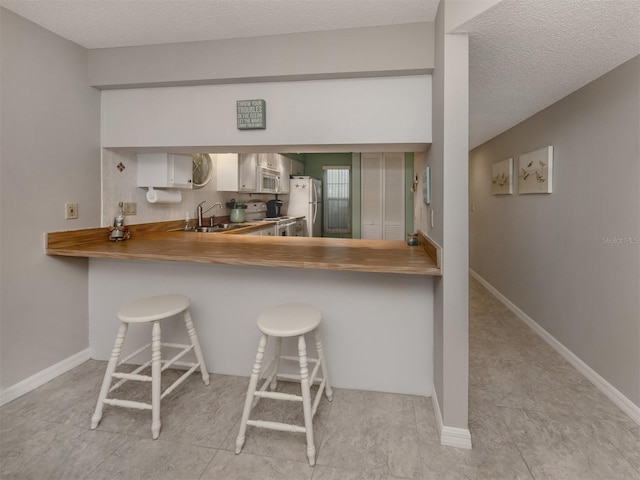 kitchen featuring sink, white appliances, white cabinets, a kitchen bar, and kitchen peninsula