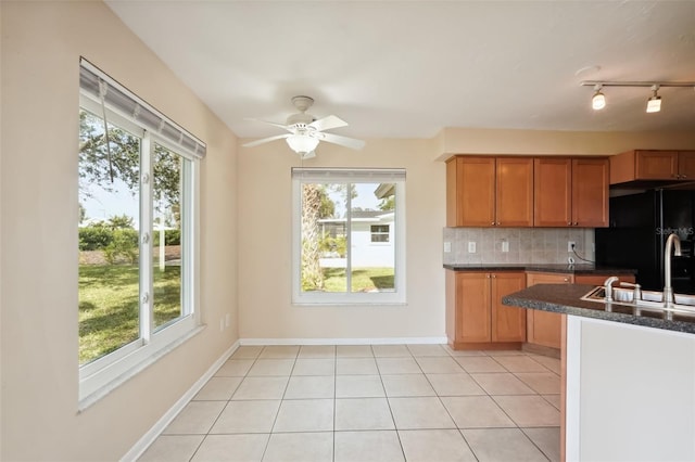 kitchen featuring light tile patterned floors, sink, backsplash, a wealth of natural light, and black fridge