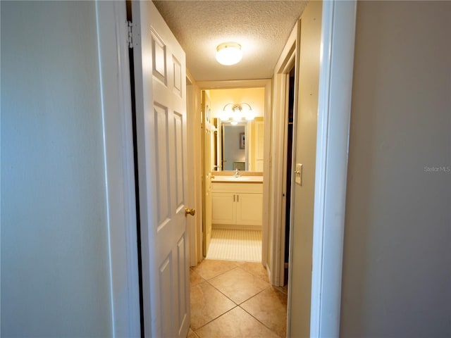 corridor featuring sink, a textured ceiling, and light tile patterned floors