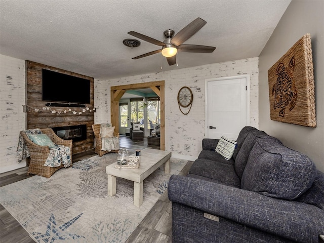 living room featuring hardwood / wood-style floors, a textured ceiling, a brick fireplace, and ceiling fan