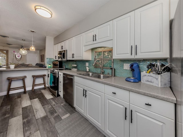 kitchen with a sink, decorative backsplash, stainless steel appliances, white cabinetry, and dark wood-style flooring