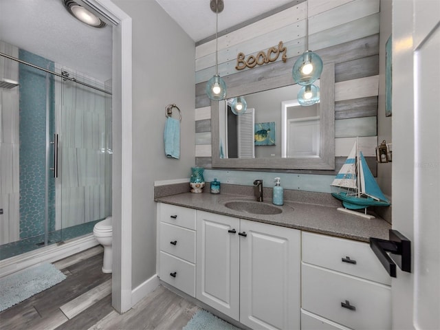 full bath featuring a shower stall, baseboards, toilet, wood finished floors, and vanity