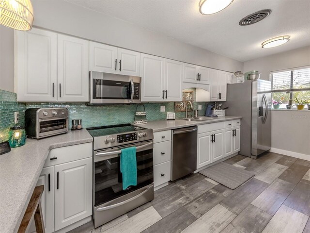 kitchen featuring visible vents, light wood-style flooring, a sink, tasteful backsplash, and stainless steel appliances