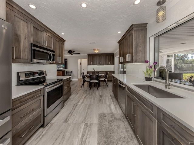 kitchen with pendant lighting, sink, stainless steel appliances, dark brown cabinetry, and a textured ceiling