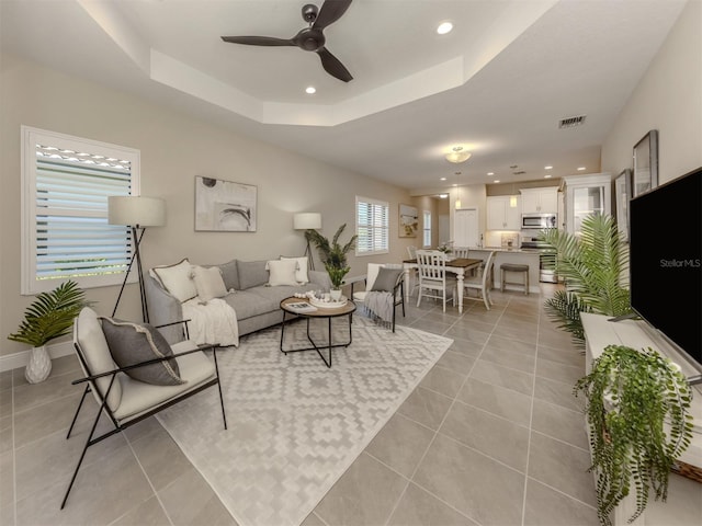 living room featuring light tile patterned floors, a raised ceiling, and ceiling fan