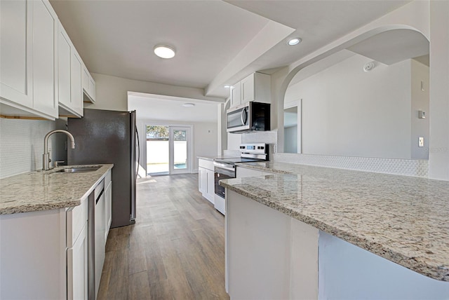 kitchen with sink, kitchen peninsula, stainless steel appliances, light stone countertops, and white cabinets