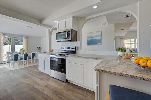 kitchen featuring light stone counters, a healthy amount of sunlight, appliances with stainless steel finishes, and white cabinets