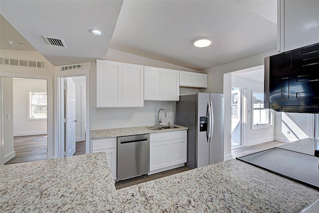 kitchen featuring appliances with stainless steel finishes, white cabinetry, lofted ceiling, sink, and light stone counters