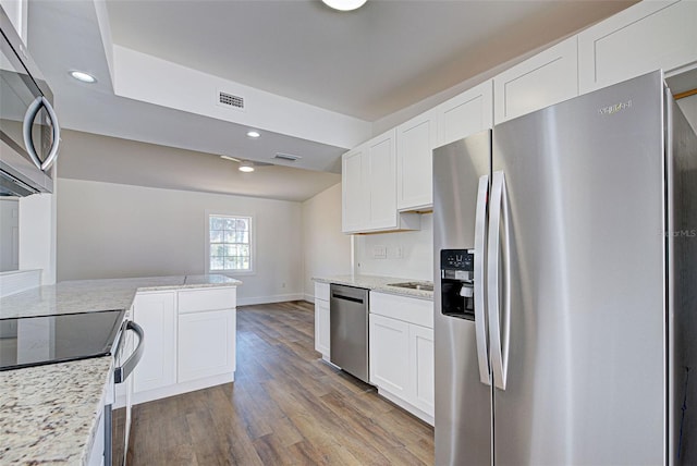 kitchen featuring vaulted ceiling, appliances with stainless steel finishes, wood-type flooring, white cabinets, and light stone counters