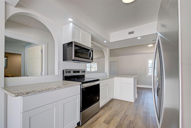 kitchen featuring appliances with stainless steel finishes, light stone counters, light hardwood / wood-style floors, white cabinets, and kitchen peninsula