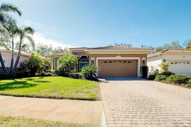 mediterranean / spanish home with a garage, a tiled roof, decorative driveway, a front yard, and stucco siding