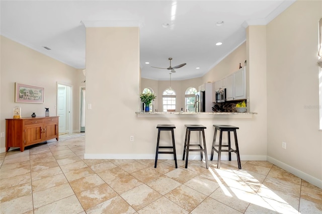 kitchen featuring a kitchen bar, appliances with stainless steel finishes, white cabinets, a peninsula, and baseboards