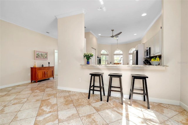 kitchen featuring a peninsula, a breakfast bar, white cabinetry, light stone countertops, and stainless steel microwave