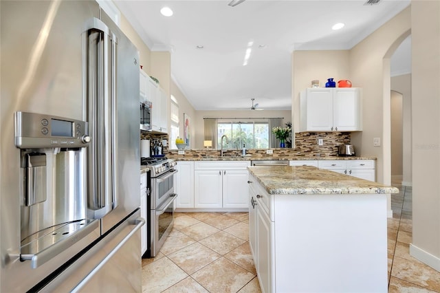 kitchen with light stone countertops, a kitchen island, white cabinets, appliances with stainless steel finishes, and decorative backsplash