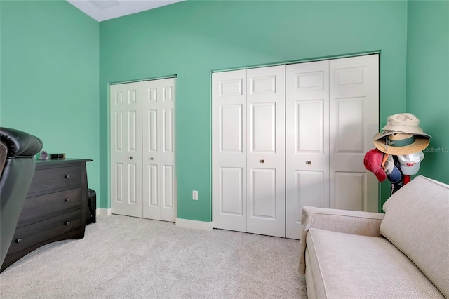 bedroom with baseboards, two closets, and light colored carpet