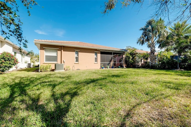 back of house with central AC unit, a lawn, a sunroom, and stucco siding