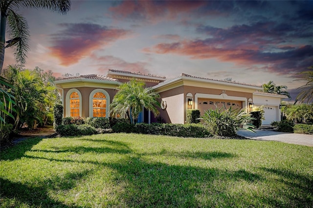 mediterranean / spanish-style home with a yard, driveway, an attached garage, and stucco siding