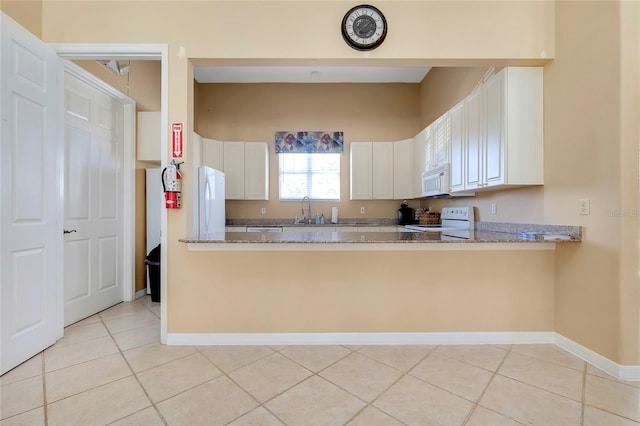 kitchen with a sink, stone counters, white appliances, white cabinets, and baseboards