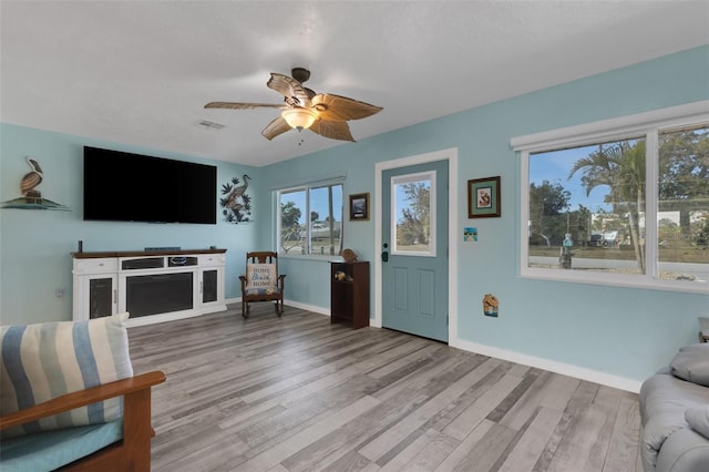 living area with light wood-style floors, visible vents, baseboards, and a ceiling fan