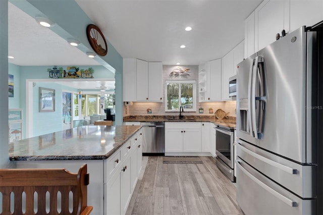 kitchen with stainless steel appliances, a sink, white cabinets, decorative backsplash, and dark stone counters