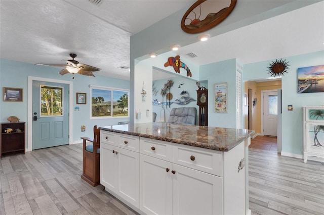 kitchen featuring light wood-style floors, white cabinetry, visible vents, and dark stone counters