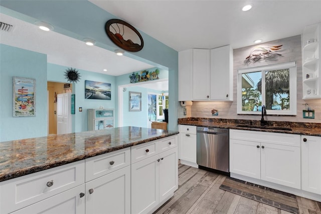 kitchen with a sink, white cabinets, stainless steel dishwasher, light wood finished floors, and dark stone countertops