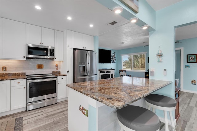 kitchen featuring visible vents, appliances with stainless steel finishes, dark stone countertops, wood tiled floor, and backsplash