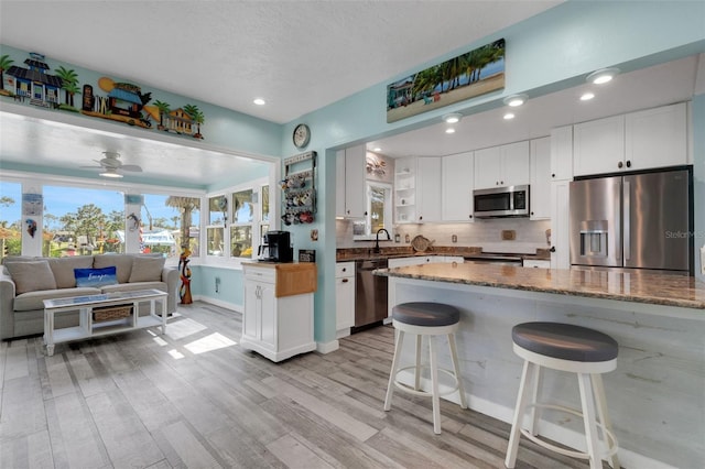 kitchen with appliances with stainless steel finishes, a breakfast bar area, dark stone countertops, and white cabinets