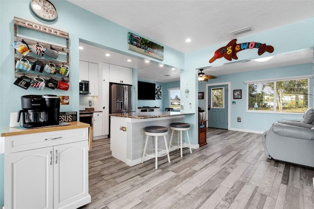 kitchen featuring visible vents, white cabinets, appliances with stainless steel finishes, open floor plan, and a kitchen breakfast bar