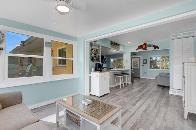 living room with light wood finished floors, ceiling fan, baseboards, and a wealth of natural light