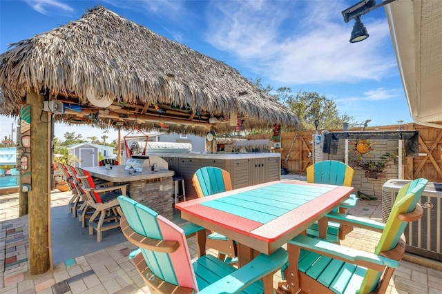 view of patio / terrace featuring outdoor dining area, central air condition unit, an outdoor structure, outdoor dry bar, and a shed