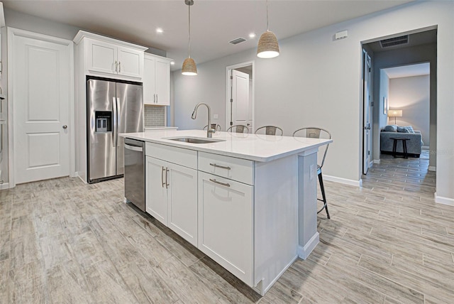 kitchen with appliances with stainless steel finishes, decorative light fixtures, sink, white cabinets, and a kitchen island with sink