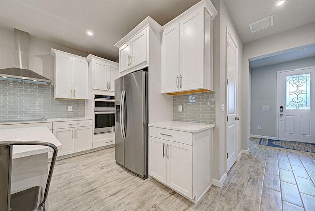 kitchen with white cabinetry, light hardwood / wood-style flooring, wall chimney exhaust hood, and appliances with stainless steel finishes