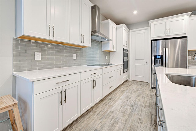 kitchen with white cabinetry, stainless steel appliances, light stone countertops, wall chimney range hood, and light hardwood / wood-style flooring