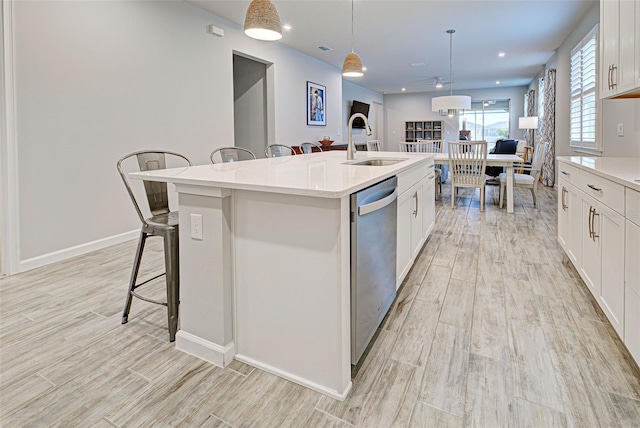 kitchen with pendant lighting, dishwasher, sink, white cabinets, and a center island with sink