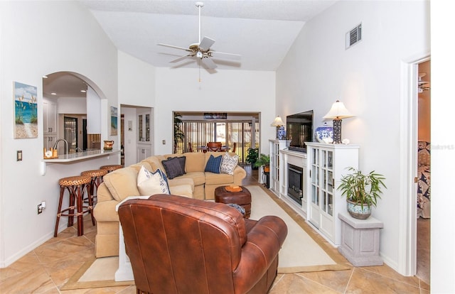 tiled living room with ceiling fan and high vaulted ceiling