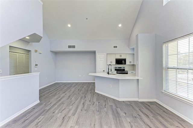 kitchen with stainless steel electric range oven, sink, white cabinets, and high vaulted ceiling