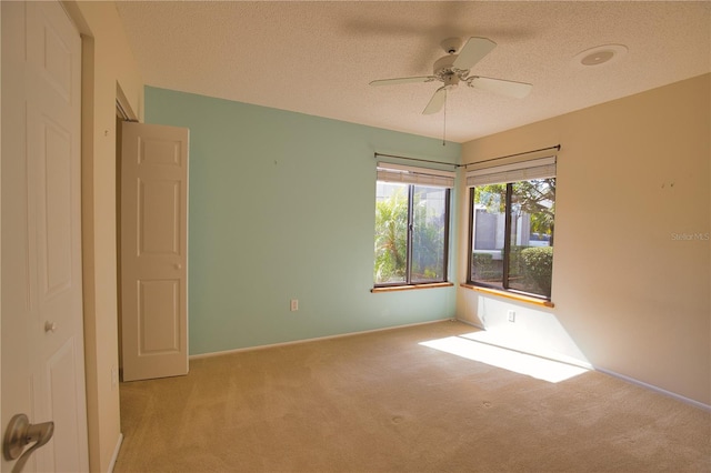 spare room featuring ceiling fan, light colored carpet, and a textured ceiling