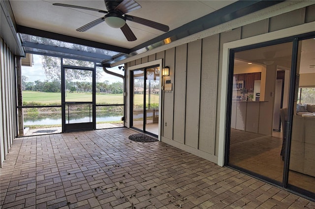 unfurnished sunroom featuring ceiling fan and a water view