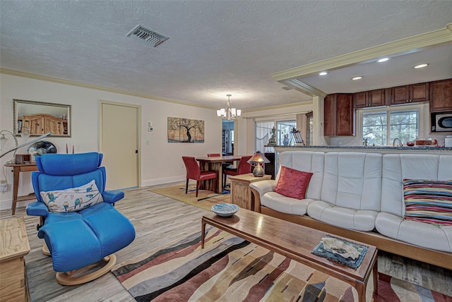 living room with crown molding, a chandelier, light hardwood / wood-style floors, and a textured ceiling